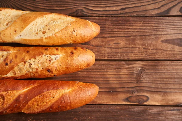 Three crispy french baguettes lie on an old wooden table with free space for text — Zdjęcie stockowe