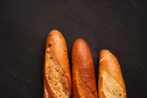 Três baguetes francesas crocantes jazem em uma mesa de madeira velha com espaço livre para texto — Fotografia de Stock