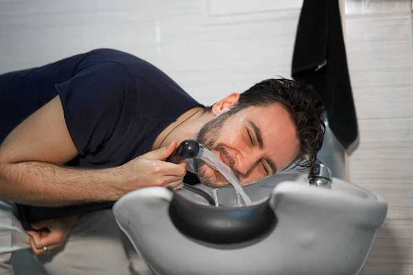 Man wash beard in beauty salon Client washing hair. Happy caucasian guy enjoy service in barbershop