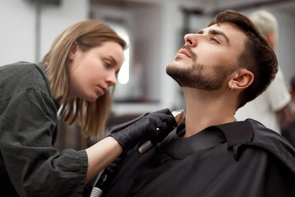 Молода красива біла жінка перукарня вирізає бороду красивого чоловіка в сучасному перукарні — стокове фото