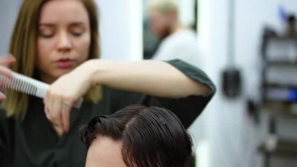 Bonito homem de olhos azuis sentado na barbearia. Cabeleireiro Cabeleireiro Mulher cortando seu cabelo. Barbeiro fêmea. — Vídeo de Stock