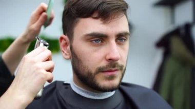 Berber dükkanında oturan yakışıklı mavi gözlü adam. Kuaför kadın onun saçını kesiyor. Kadın berber.. 