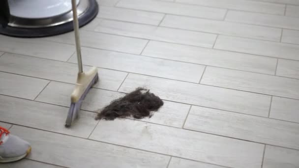 Cheveux courts noirs masculins se trouve sur le sol près du fauteuil de salon de coiffure du coiffeur après une coupe de cheveux . — Video