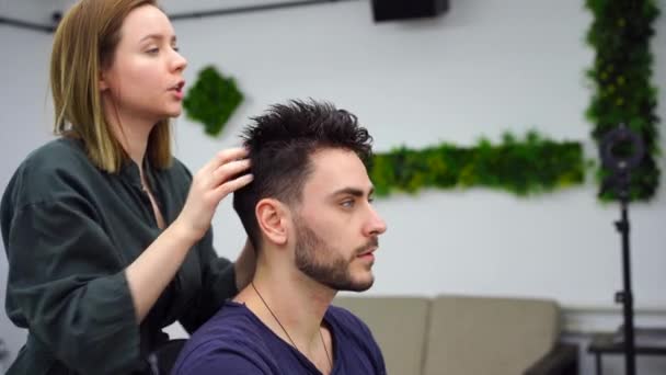 Hombre guapo de ojos azules sentado en la peluquería. Peluquera Peluquera cortándole el pelo. Peluquero femenino. — Vídeos de Stock