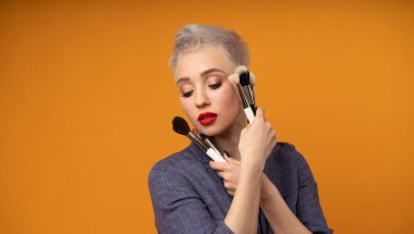 Portre makyözünü kapat. Kursları hazırla. Kişisel görünüm ana sınıflandırması kavramı. Moda uzmanı. Kadın elinde makyaj fırçası tutuyor. Turuncu arkaplanda stüdyo çekimi