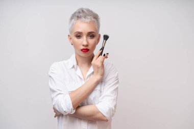 Portre makyözünü kapat. Kursları hazırla. Kişisel görünüm ana sınıflandırması kavramı. Moda uzmanı. Kadın elinde makyaj fırçası tutuyor. Beyaz arkaplanda stüdyo çekimi