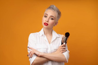 Portre makyözünü kapat. Kursları hazırla. Kişisel görünüm ana sınıflandırması kavramı. Moda uzmanı. Kadın elinde makyaj fırçası tutuyor. Turuncu arkaplanda stüdyo çekimi