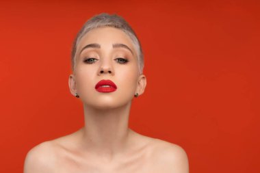 Renkli turuncu arka planda kısa saçlı, kırmızı dudaklı, çıplak omuzlu, moda portresi yapan kadını kapat..