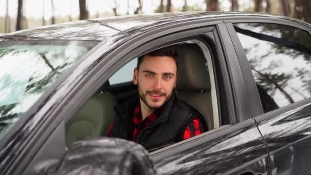Junger attraktiver Mann aus dem Kaukasus sitzt an einem sonnigen Wintertag am Steuer seines Autos. — Stockvideo