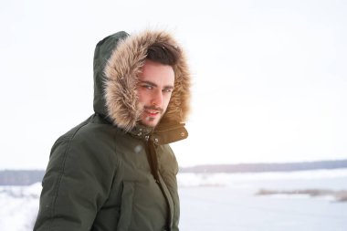 Yakışıklı, sakallı, beyaz, açık havada kürklü, kışlık donmuş bir göl. Çekici stil sahibi Avrupalı adam, karlı Noel ormanlarında yürüyor.                       