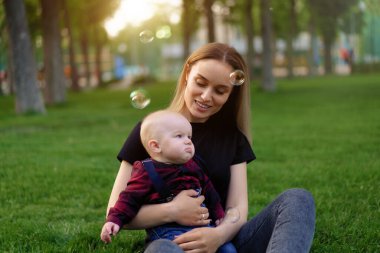 Genç beyaz anne güneşli bir yaz gününde oğluyla birlikte parkta sabun köpüklerini şişiriyor. Mutlu aile tatilleri.