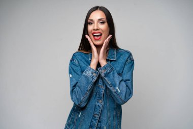 Beyaz arka planda stüdyoda poz veren güzel beyaz kadın kot ceketi. Baştan çıkarıcı esmer. Denim tarzı kırmızı dudaklar zarif makyaj. Kapıda duran genç kadın şaşırdı ve hayran kaldı.