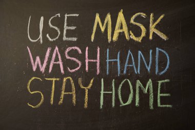 Maskeni tak ve ellerini yıka. Evde kal Salgın Uyarısı. Dünya çapındaki koronavirüs salgınıyla ilgili olarak tahtaya beyaz tebeşir yazılmış. Siyah arkaplan ve boş alan üzerine Covid 19 pandemik metin.