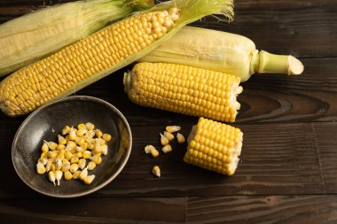 Yeşil yaprakları ile mısır koçan masada yatıyor. Koyu ahşap arka plan. Metin için alan kopyalama.