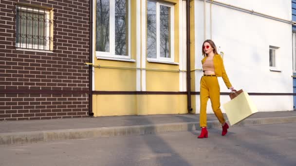 Een jonge Kaukasische Europese meisje Shopaholic wandelen langs de straat met aankopen in pakketten. — Stockvideo