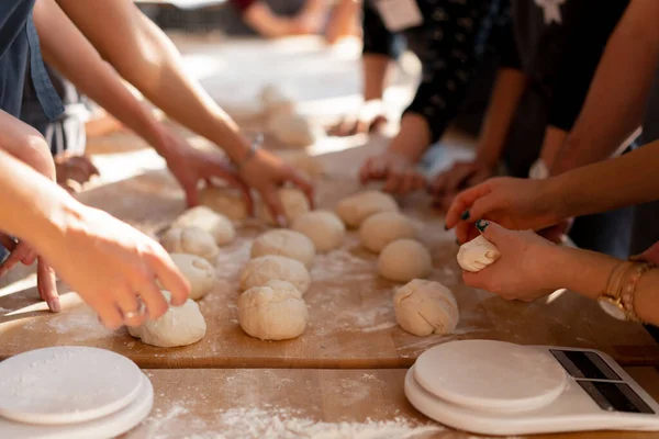 Close-up hands forming dough balls for baking buns on a wooden table during manufacture. Culinary master classes. A large unrecognizable family prepares dough for baking. Hands close up