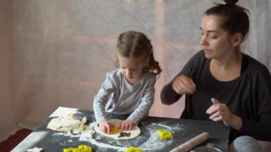 Küçük sevimli beyaz kız. 3 yaşında annesiyle birlikte. Evde çiğ hamurdan kurabiye hazırlıyor..