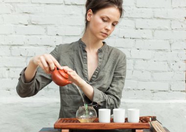 Arka planında beyaz tuğla duvar olan Oryantal çay seremonisi ustası. Gri gömlekli bir kadınla geleneksel çay partisi. Güzel kadın geleneksel çay seremonisini hazırla.