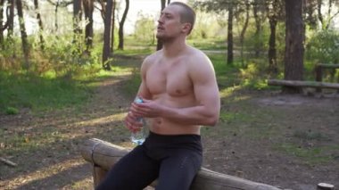 Atletizm sporcusu ağaç ormanına dayanmış plastik şişe egzersizi içer.