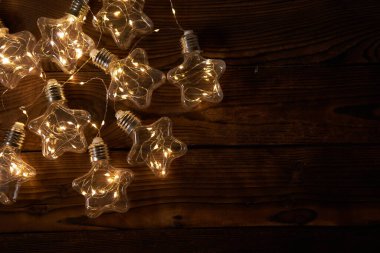 Yıldızların şeklindeki parlak Noel çelenkleri koyu ahşap bir arka planda yatar. Kopyalama alanı olan yeni yıl ışığı