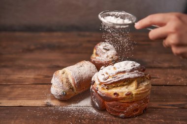Geleneksel Paskalya pastası Kraffin, koyu bir arka plan karşısında ahşap masanın üzerinde duruyor. Fotokopi alanı olan bahar tatili ekmeği Aşçı pudra şekeriyle serpiştirir