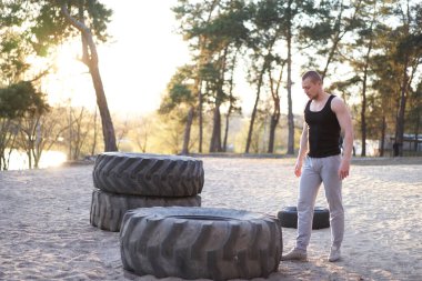 Güçlü adam spor yapıyor. Geniş lastik kaldırıyor. Spor salonu. Sportif, genç, beyaz bir adam doğada büyük çarklar çeviriyor. El yapımı ekipman sporu Helthy yaşam tarzı konsepti