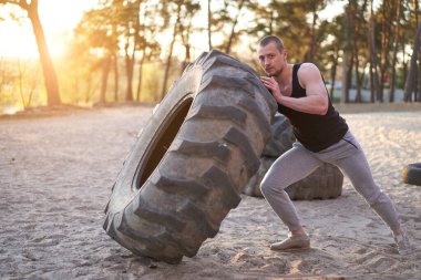Güçlü adam spor yapıyor. Geniş lastik kaldırıyor. Spor salonu. Sportif, genç, beyaz bir adam doğada büyük çarklar çeviriyor. El yapımı ekipman sporu Helthy yaşam tarzı konsepti
