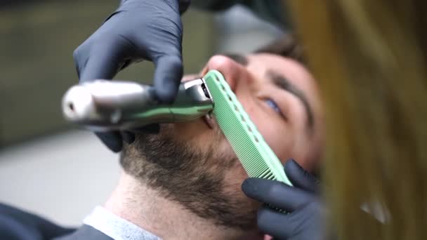 Ung smuk kaukasisk kvinde frisør skærer skæg smuk mand på moderne barbershop – Stock-video