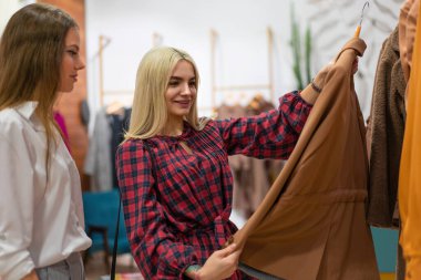 Moda butiği olan iki kadın sonbahar sezonu için palto seçiyor. Profesyonel stilist, müşterilere kıyafet seçmede yardımcı oluyor. Tatil alışverişi indirimleri iki beyaz kız arkadaş alışveriş merkezinde yürüyor.