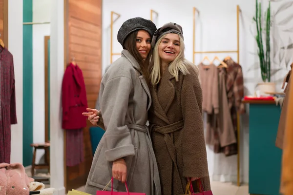 Two women in fashion boutique choose coat for autumn season A professional stylist helps customers choose clothes. Season holiday shopping discounts sale two caucasian girlfriends walk shopping mall