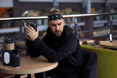 Genç yakışıklı, yalnız bir adam kafeterya masasında oturmuş, üzgün bir şekilde buluşmayı bekliyor ve kağıt bardaktan kahve içiyor. Siyah kapüşonlu bandana giyen beyaz adam kendini yalnız hissediyor.. 