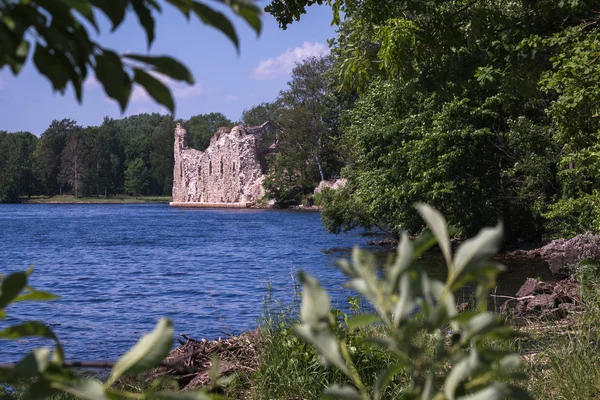 ancient historical ruins on the water\'s edge; blue river water, there are big trees all around. Sunny day with blue sky.