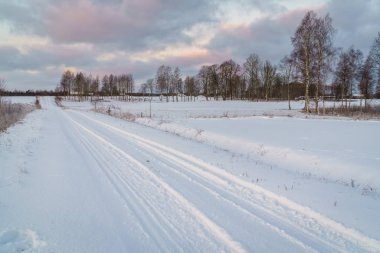 Kış sabahı, kır yolu ve karla kaplı tarlalar, uzakta tepe manzarası görebilirsiniz..