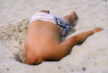 a boy digs a deep hole in the sand with his hand, his head is invisible, it is underground