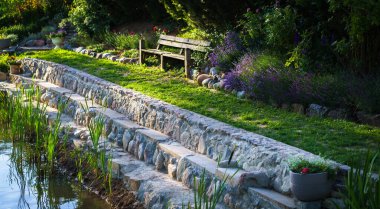 Kaya ve beton basamakların kıyı takviyesi; göl kenarındaki bahçe oturma alanı