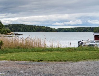 İsveç 'teki Baltık Denizi manzarası, kıyı sazlıkları ve ön planda bir tekne rıhtımı, ormanı görebilirsiniz.