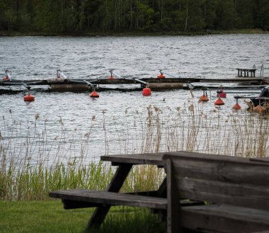 Kırmızı şamandıralarda demir atan kayıklar. Yaz günü, karşı kıyıdaki orman.