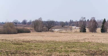 Uzakta dolambaçlı bir köy yolu var, hemen yanında yaprakları olmayan tarlalar ve ağaçlar var.