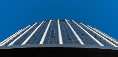 Ön tarafında mavi camdan pencereler olan büyük bir bina. Mavi gökyüzüne karşı taban manzaralı.