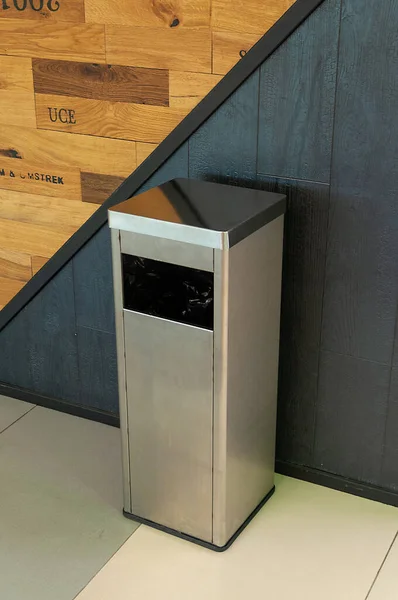 steel-colored trash can against the black wall