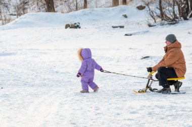 Petrozavodsk, Rusya - 29 Şubat 2020. Kız babasını kar motosikletine bindirmeye çalışıyor.
