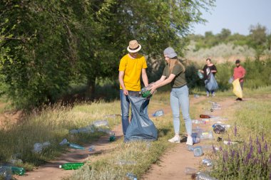 Teenagers collect plastic bottles to trash bags on the forest road. clipart