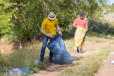 Two young men collect plastic bottles into trash bags. clipart