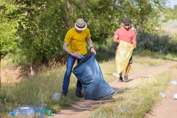 Two young men collect plastic bottles into trash bags.