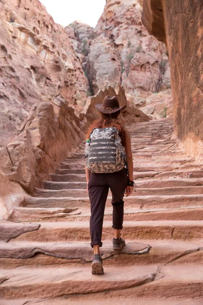 一个背着背包 头戴牛仔帽的女旅行家爬上了一座用石头雕刻的古老楼梯 — 图库照片