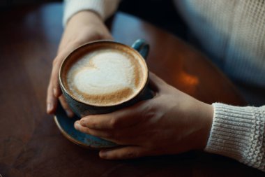 Genç adam elinde kalp şeklinde köpüklü bir latte tutuyor.