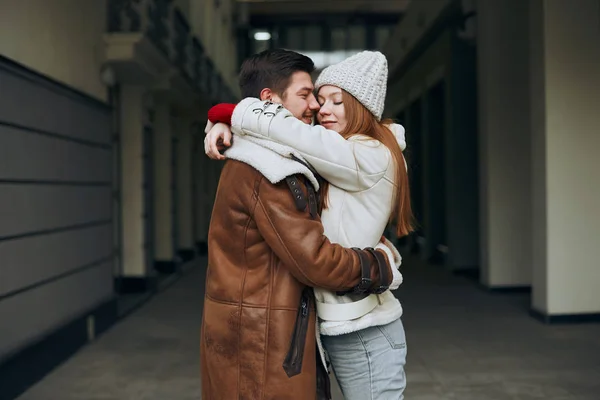 Feliz jovem casal incrível em casacos abraçando na rua da cidade — Fotografia de Stock