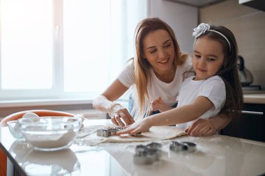 smiling blonde woman helping her child to cut figures