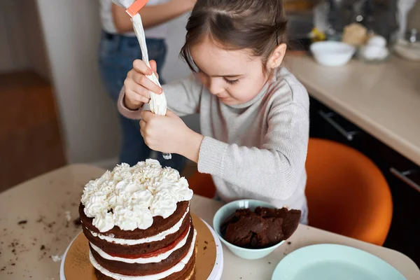 Criança espremendo creme de saco de pastelaria no topo do bolo — Fotografia de Stock