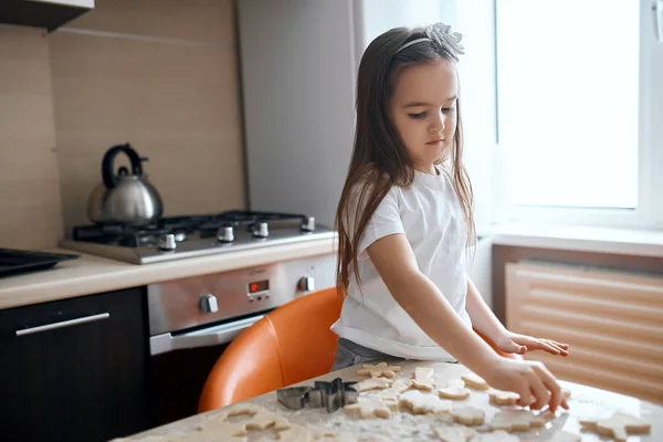Pequena menina com cabelos longos castanhos lisos preparando biscoitos — Fotografia de Stock